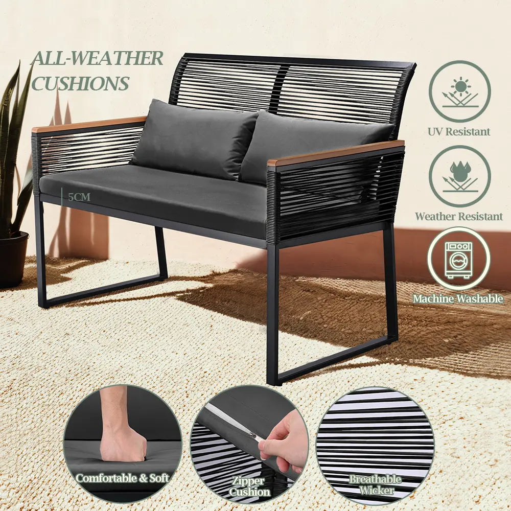 Black rattan loveseat and side table placed on a patio with greener